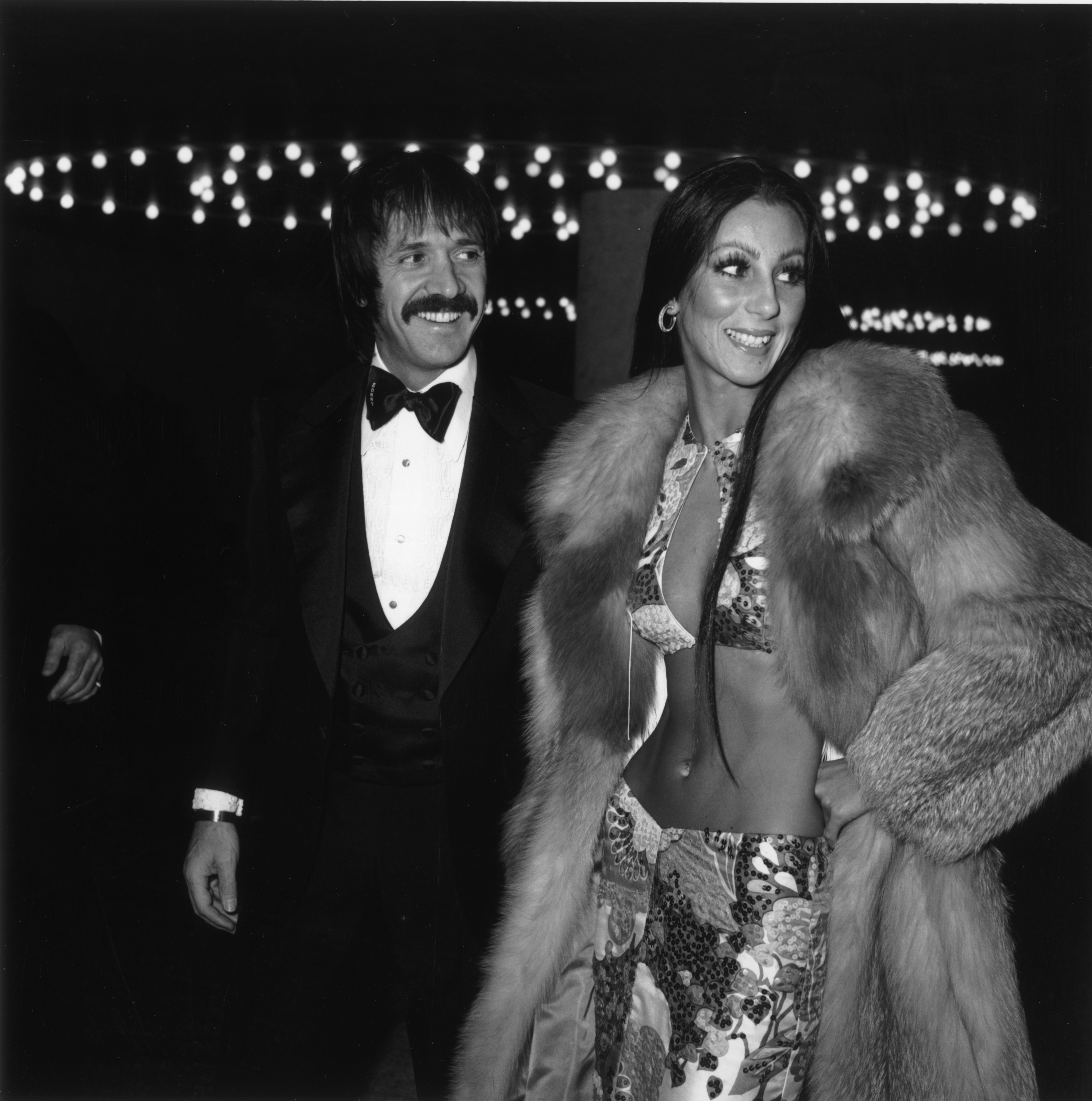 1973: American singers Sonny and Cher attend the Golden Globe Awards, Los Angeles, California. Sonny Bono (1935 - 1998) wears a tuxedo; Cher wears a midriff-baring two piece outfit and fur coat. (Photo by Max B. Miller/Fotos International/Getty Images)