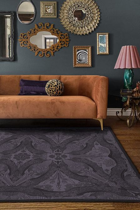 A living room with a velvet couch, a printed rug, a bold table lamp, and an ornate gallery wall