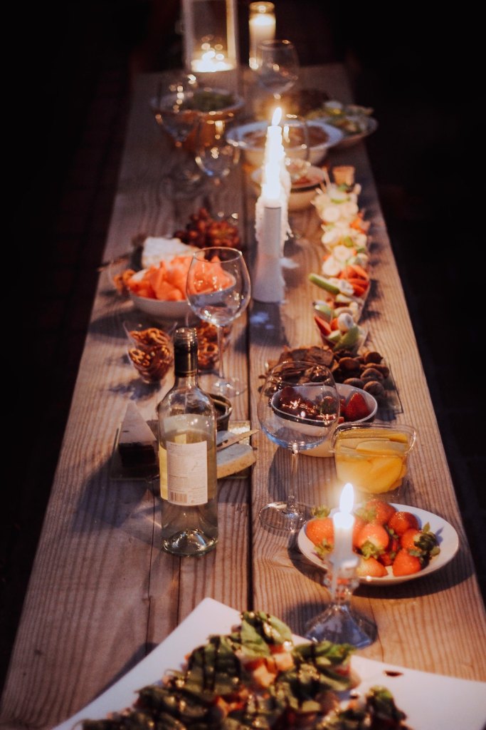 An outdoor dining table topped with food, wine, and candles