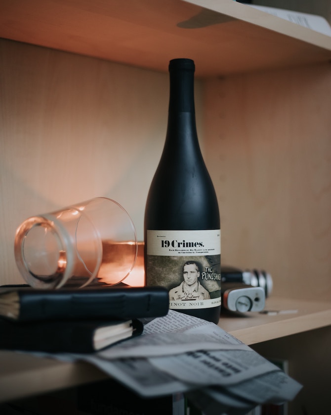A bottle of 19 Crimes wine on top of a stack of books and a newspaper