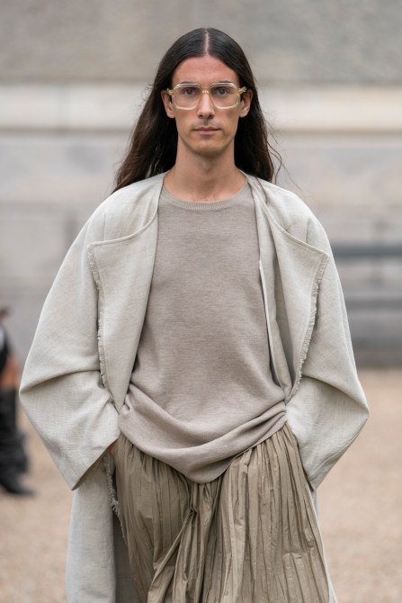 Runway model wearing neutral-toned outfits and transparent glasses.