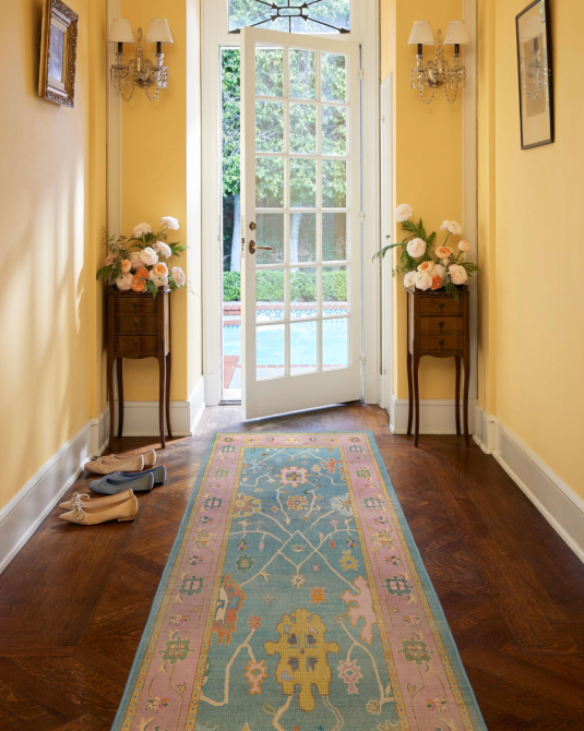 An entryway with yellow walls, antique furniture, and a blue and pink printed rug