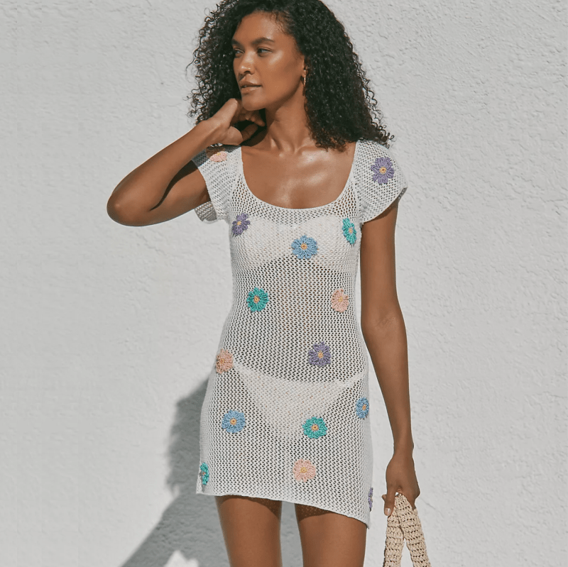 A model wearing a white crochet mini dress over a bathing suit