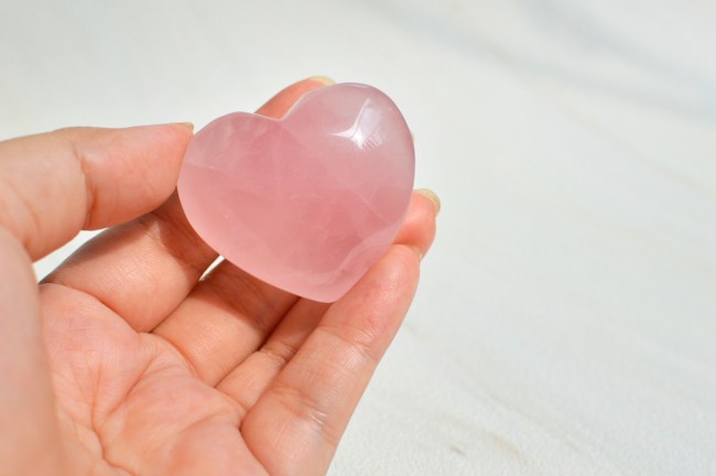 Hand holding a heart-shaped rose quartz crystal
