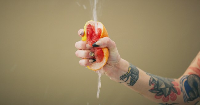 Studio shot of an unrecognizable woman squeezing a grapefruit slice against a brown background