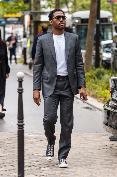 A man wears grey suit, white t-shirt, black sneakers,