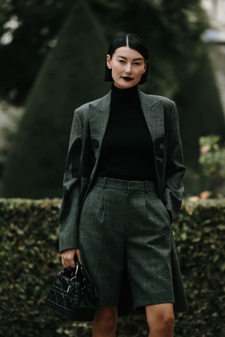A woman wears a black turtleneck top with a gray blazer and matching long shorts.
