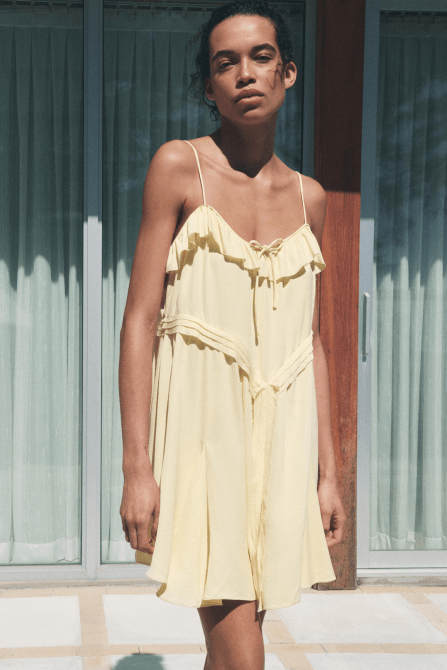A model wearing the Zara Short Ruffle Dress in butter yellow